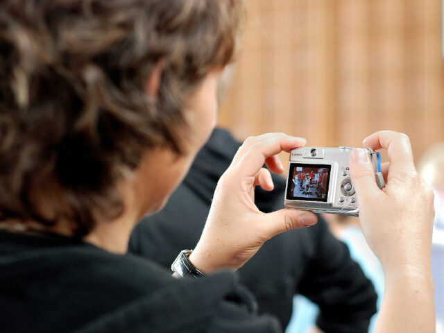 Peron hält Digitalkamera und macht ein Foto